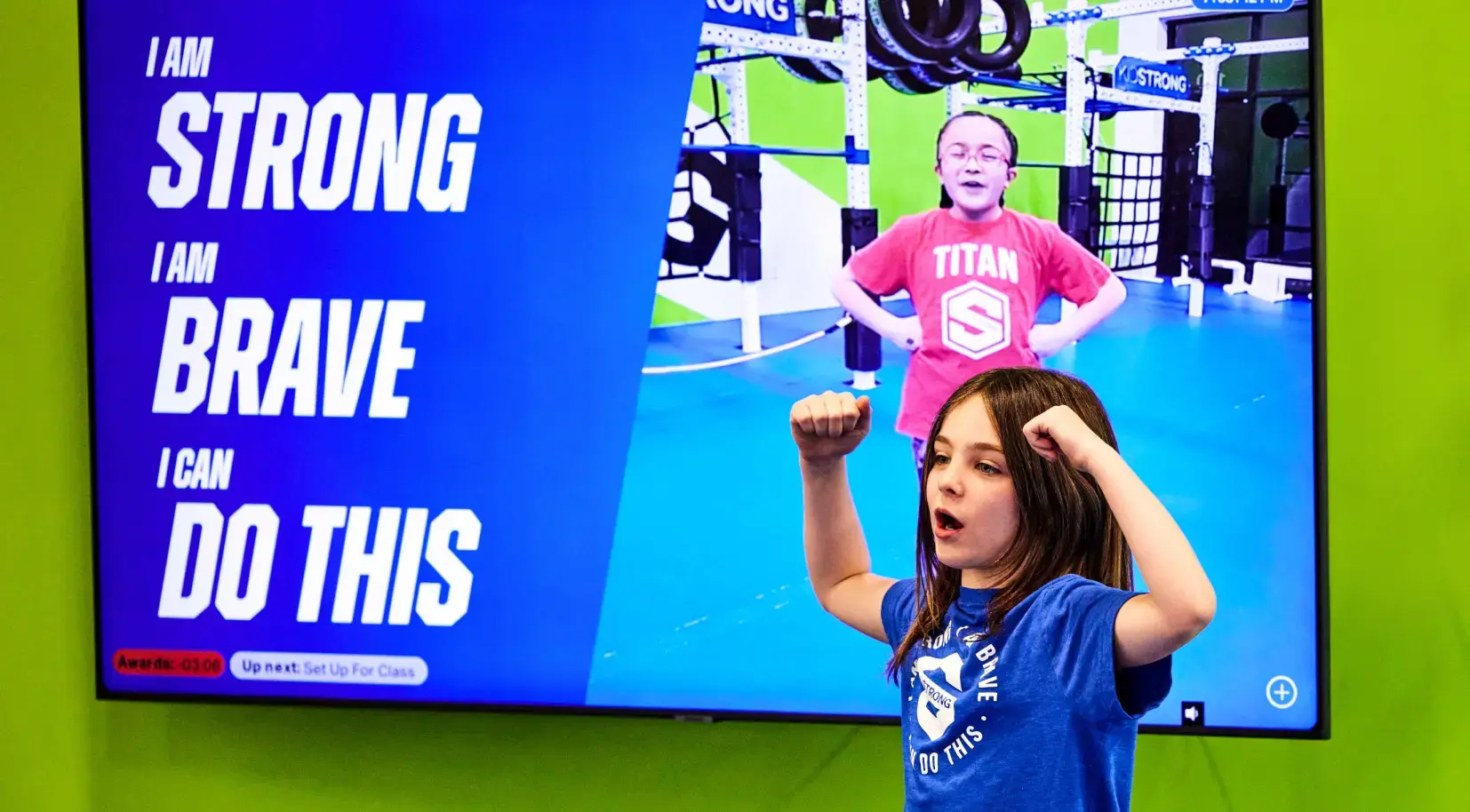 Student with arms flexed in front of a screen that says 'I am STRONG, I am BRAVE, I can DO THIS'