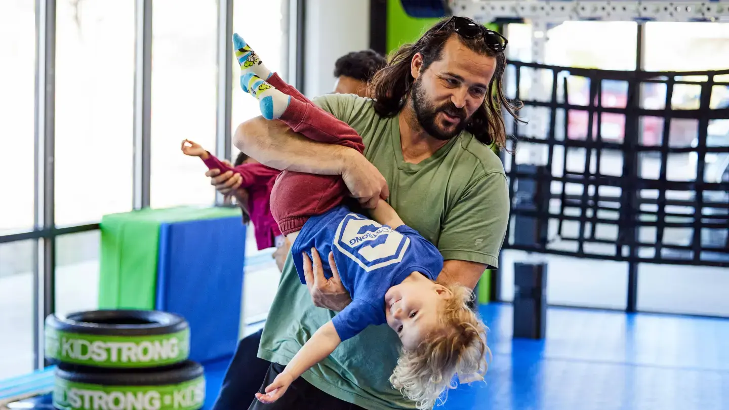 A KidStrong parent having fun participating by carrying their child for a class activity.